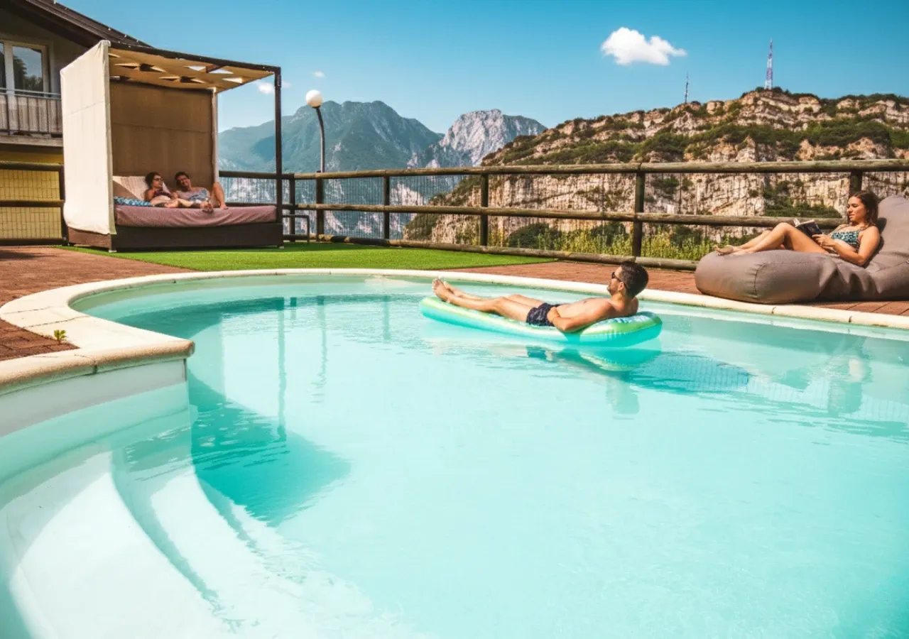 La piscina con gli ospiti: una coppia sul lettino a baldacchino, un ragazzo sul materassino e le montagne dietro
